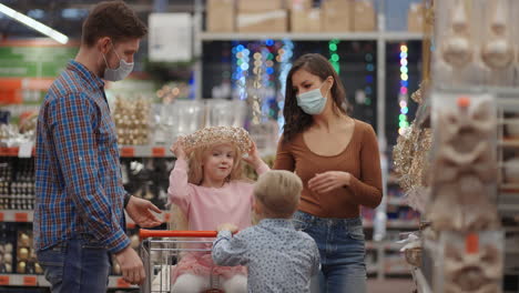 A-married-couple-with-two-children-in-a-shopping-center-in-protective-masks-in-the-coronavirus-epidemic-are-preparing-for-Christmas-and-choosing-decorations